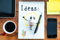 Top view of note pad with Idea text, and coffee cup laying on the wooden desk with different business stuff around it - Simple Ideas to Increase Productivity
