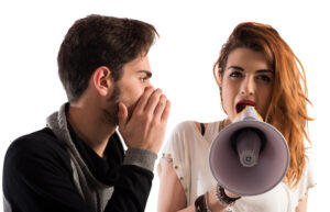 Woman shouting into a megaphone at a man talking quietly in her ear  - Ways to Deal with Difficult People