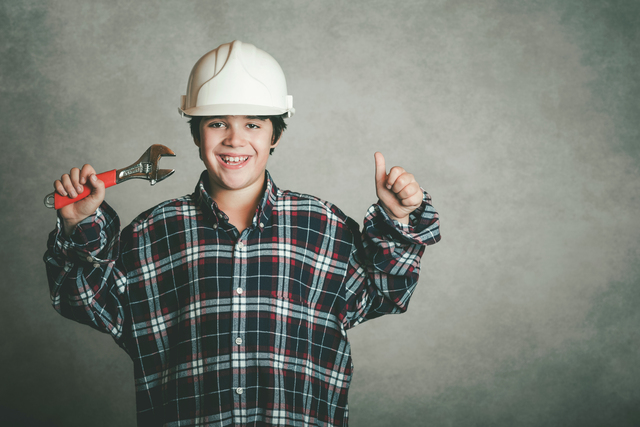 Smiling boy with a white helmet holding a wrench - Member of a family owned plumbing business - Family owned business challenges