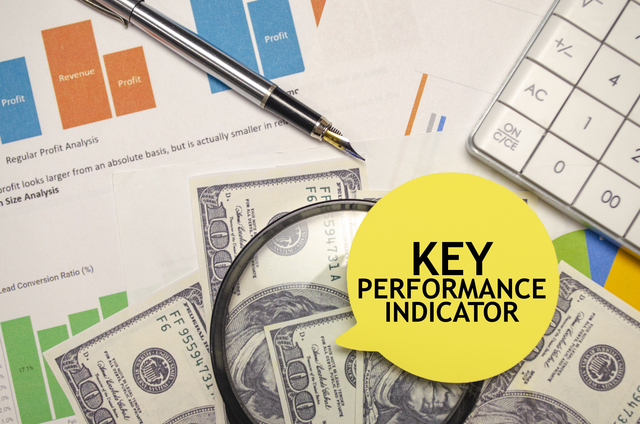 Key-performance-indicator-words-on-yellow-sticker-with-hundred-dollar-notes- charts-calculator-and-a-pen - Define Business Objectives