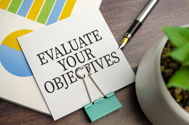 Notebook with text EVALUATE YOUR OBJECTIVES on charts -How to Expand a Small Business