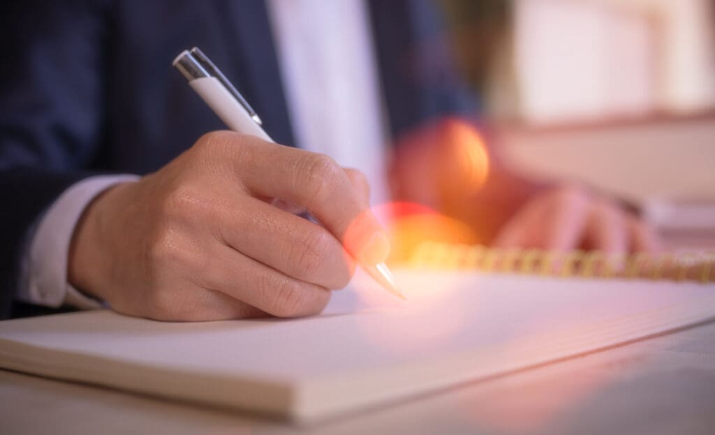 businessman-writing-on-notebook-in-office-on-table - Guide to Writing Mission and Vision Statements